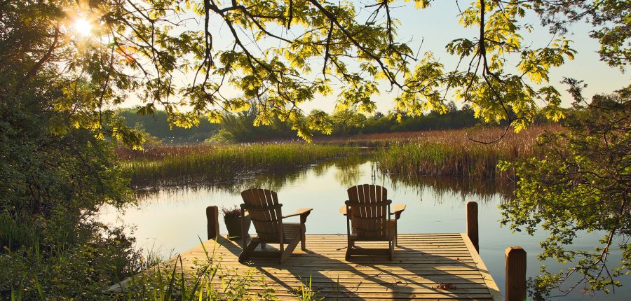 A pair of adirondack chairs facing a placid pond at sunset.