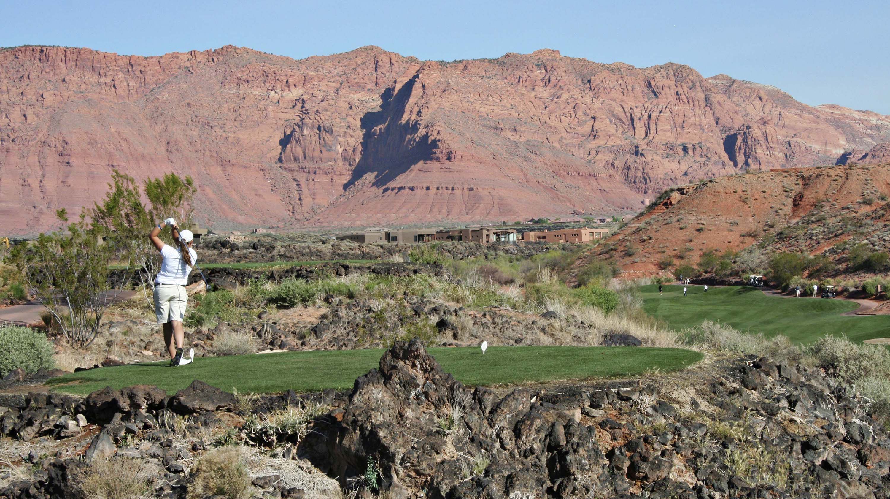 A woman swings a golf club in a desert environment.