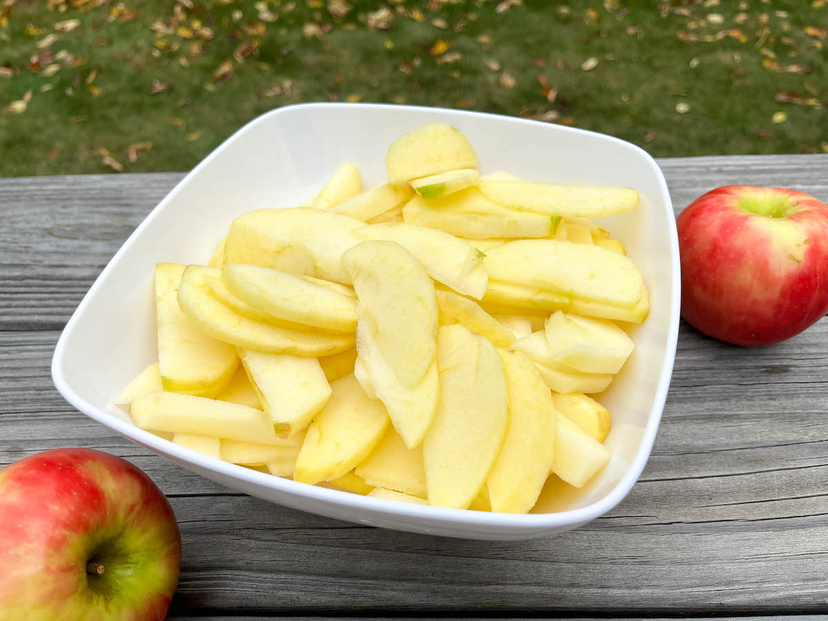 Sliced apples in a white bowl on wooden table.