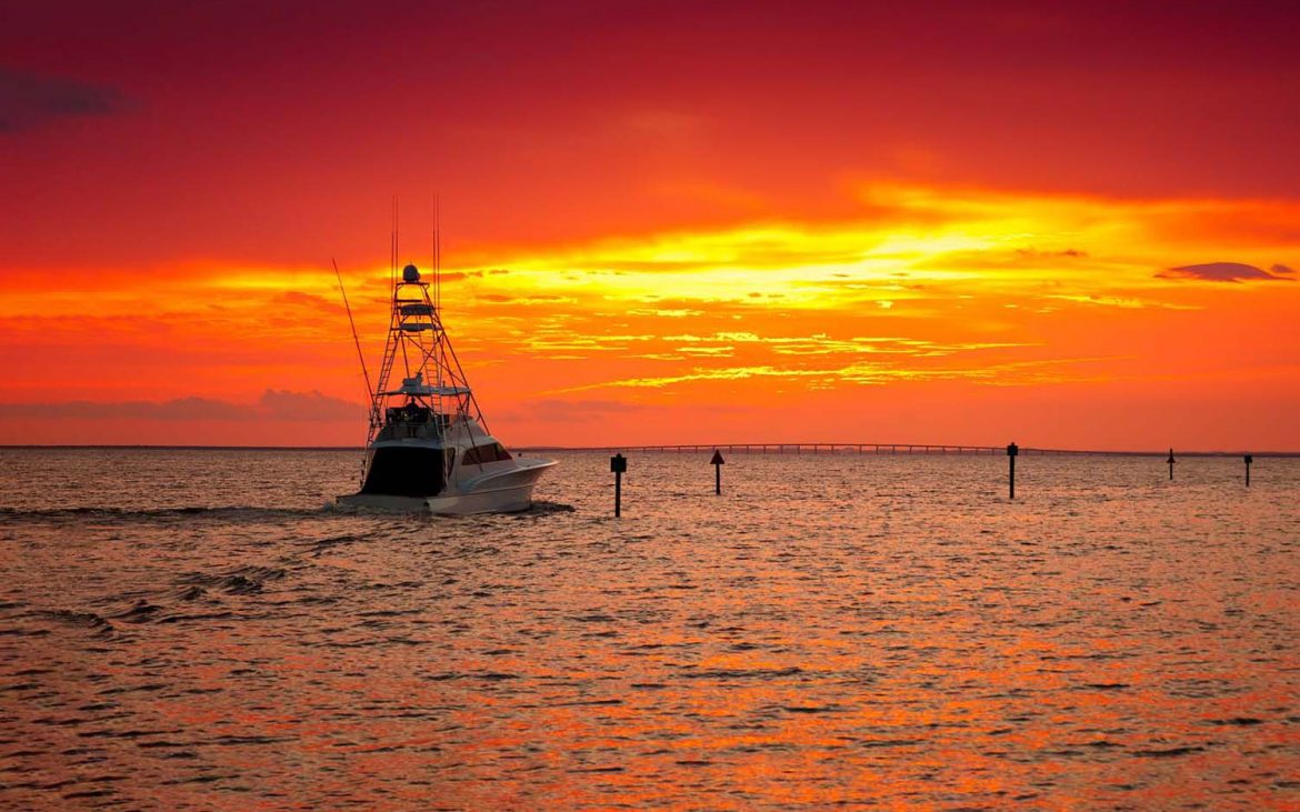 A fishing boat headed toward sunset under a red sky.