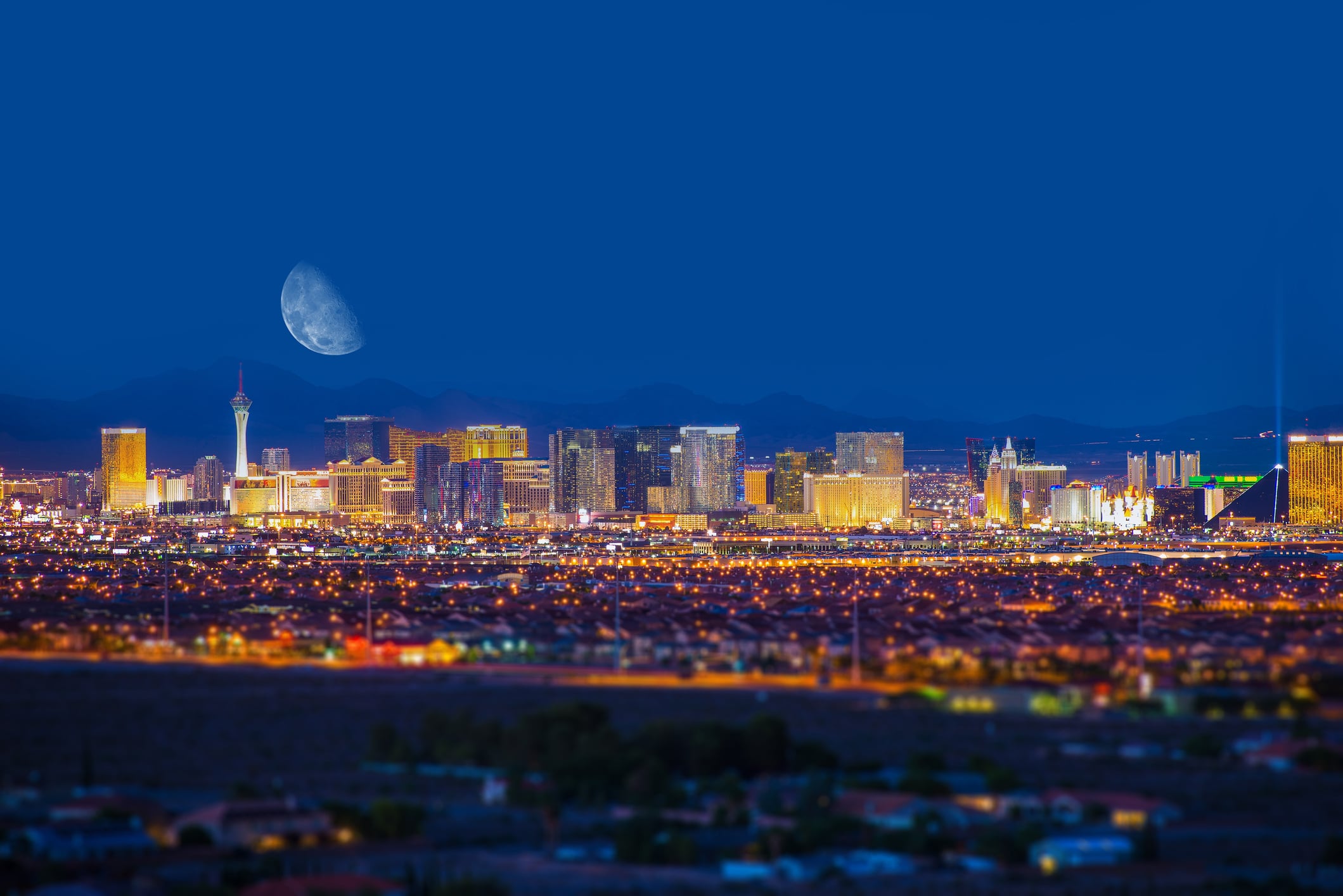 Moon hangs low over brightly lit Vegas skyline.