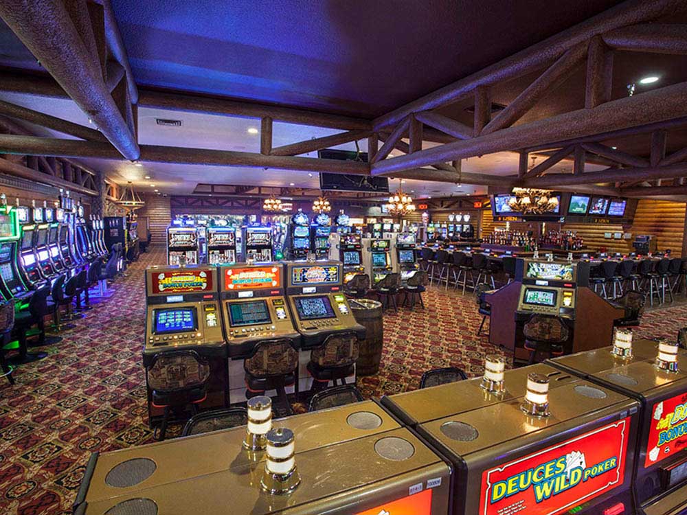 Slot machines and poker games glow in a casino with wooden frame supports.