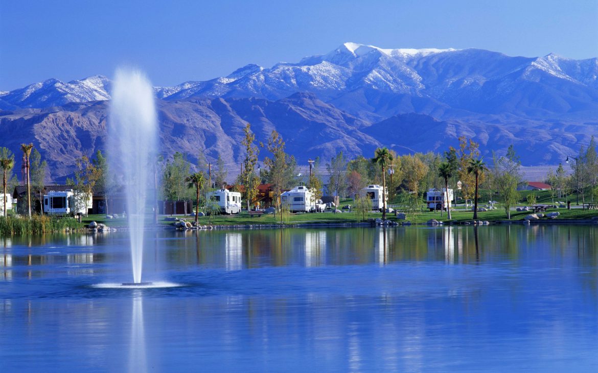 A fountain gushes on the lake with RVs parked in a row in the background.