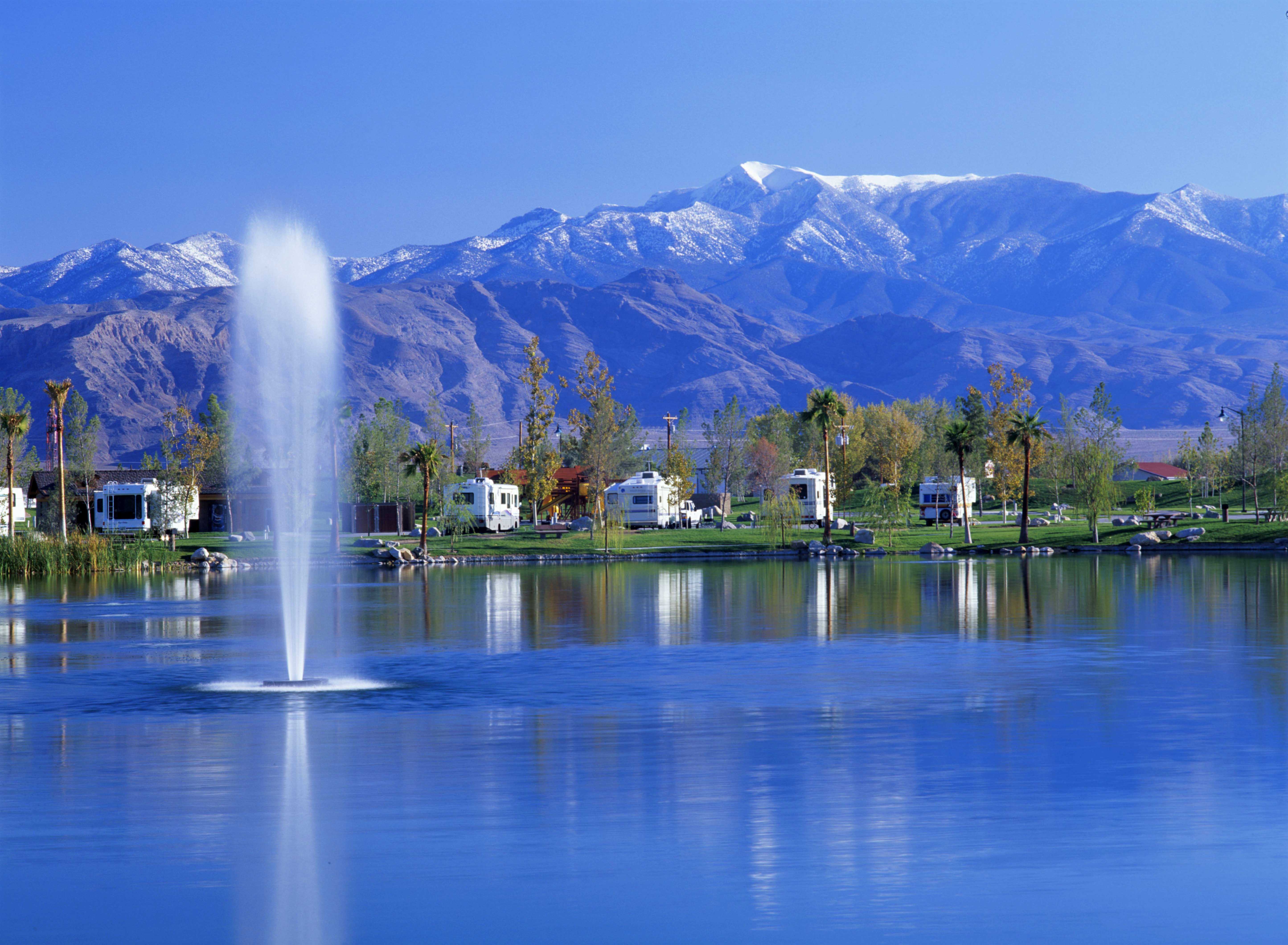 A fountain gushes on the lake with RVs parked in a row in the background.