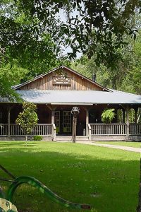 Country Oaks RV Park and Campground —A homey wooden building on a lush green lawn.
