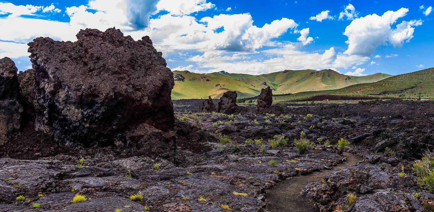 Rocky cooled lava terrain with green hills on the background.