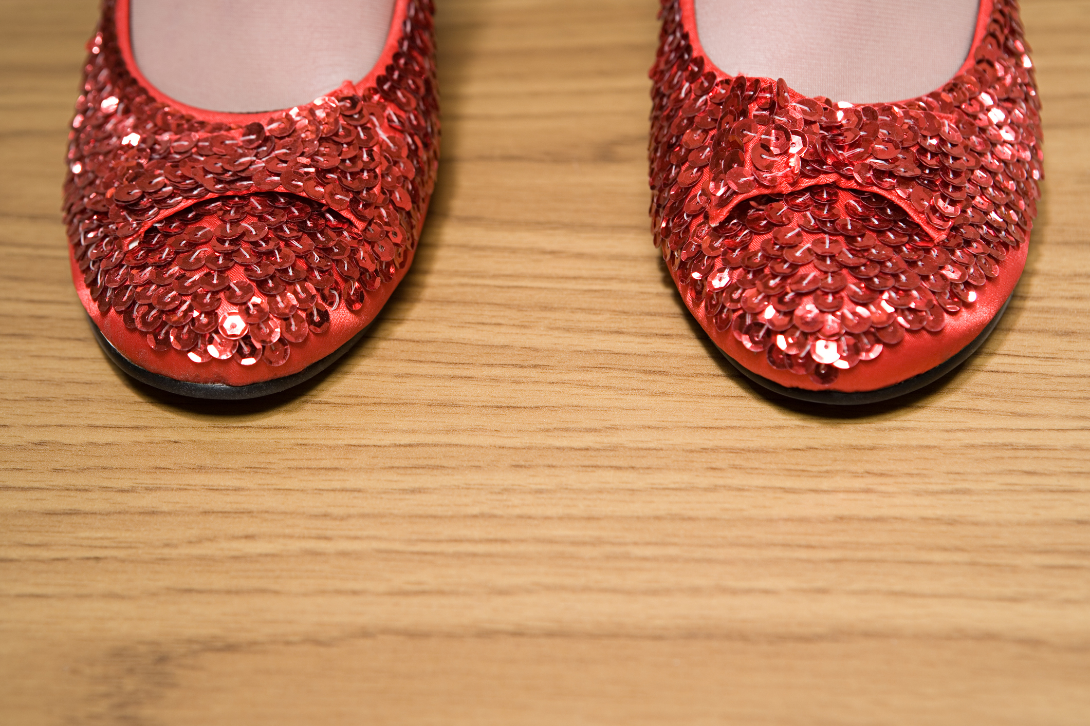 A pair of sparkly ruby red slippers on a wood surface.