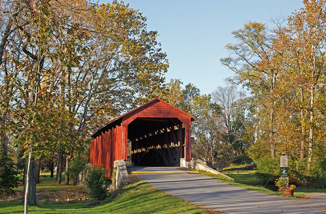 Fall trees flank a red covered bridge.