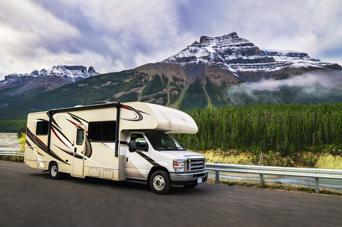 A Class C motorhome driving past a snow-dusted mountain.