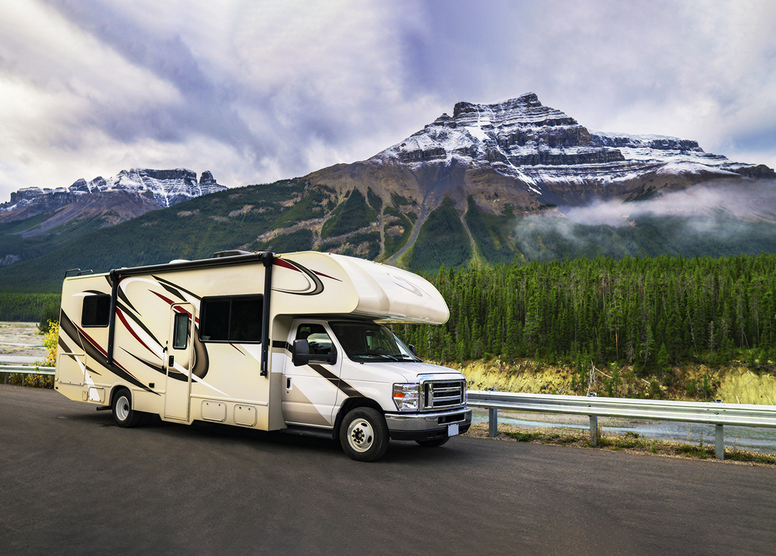 A Class C motorhome driving past a snow-dusted mountain.
