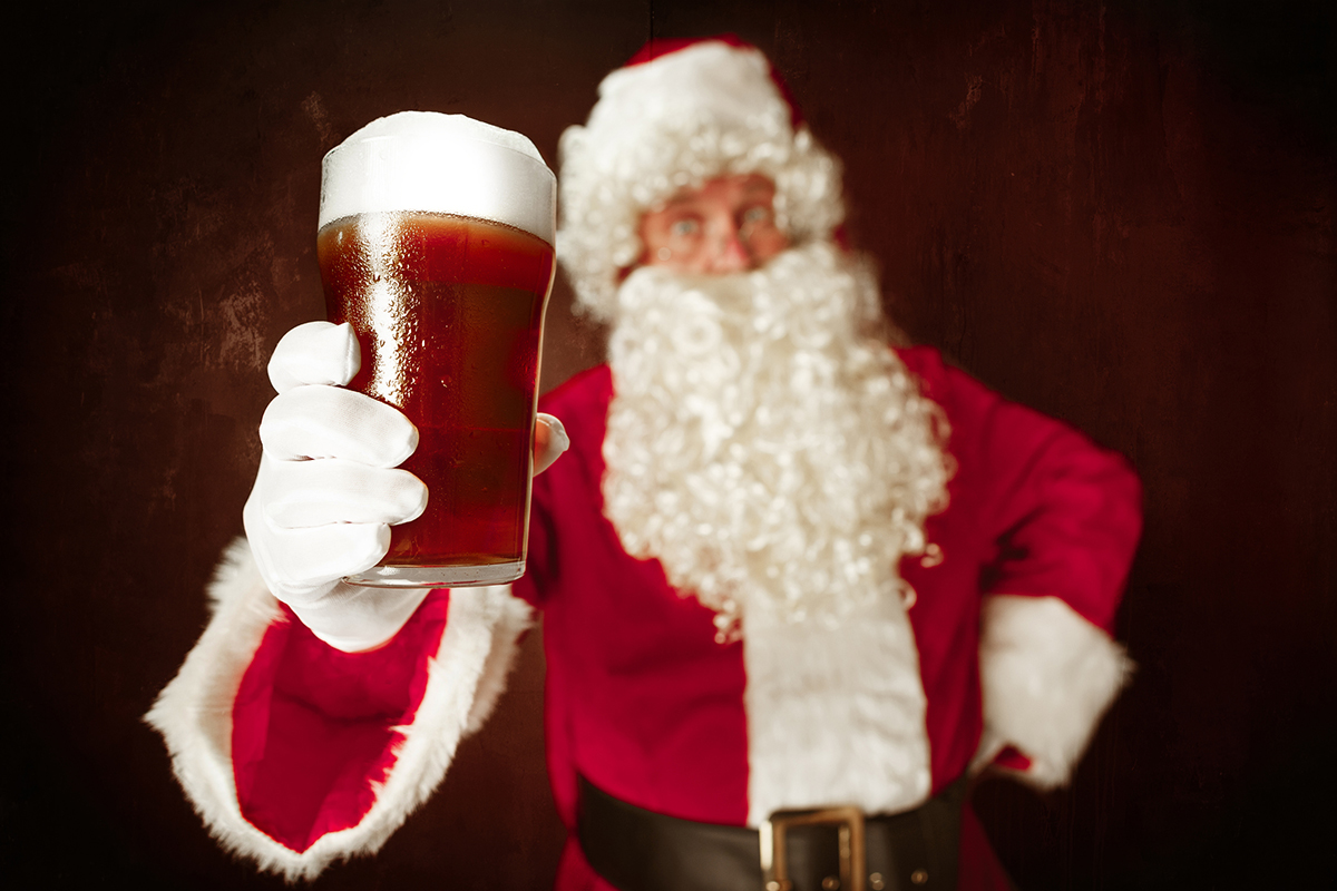 Man in Santa outfit hefts a tall glass of ale.