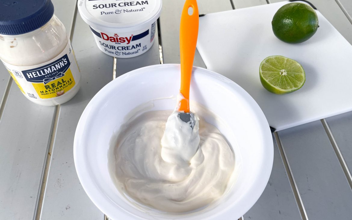 Mayonnaise, limes, sour cream and other ingredients arrayed around a bowl.