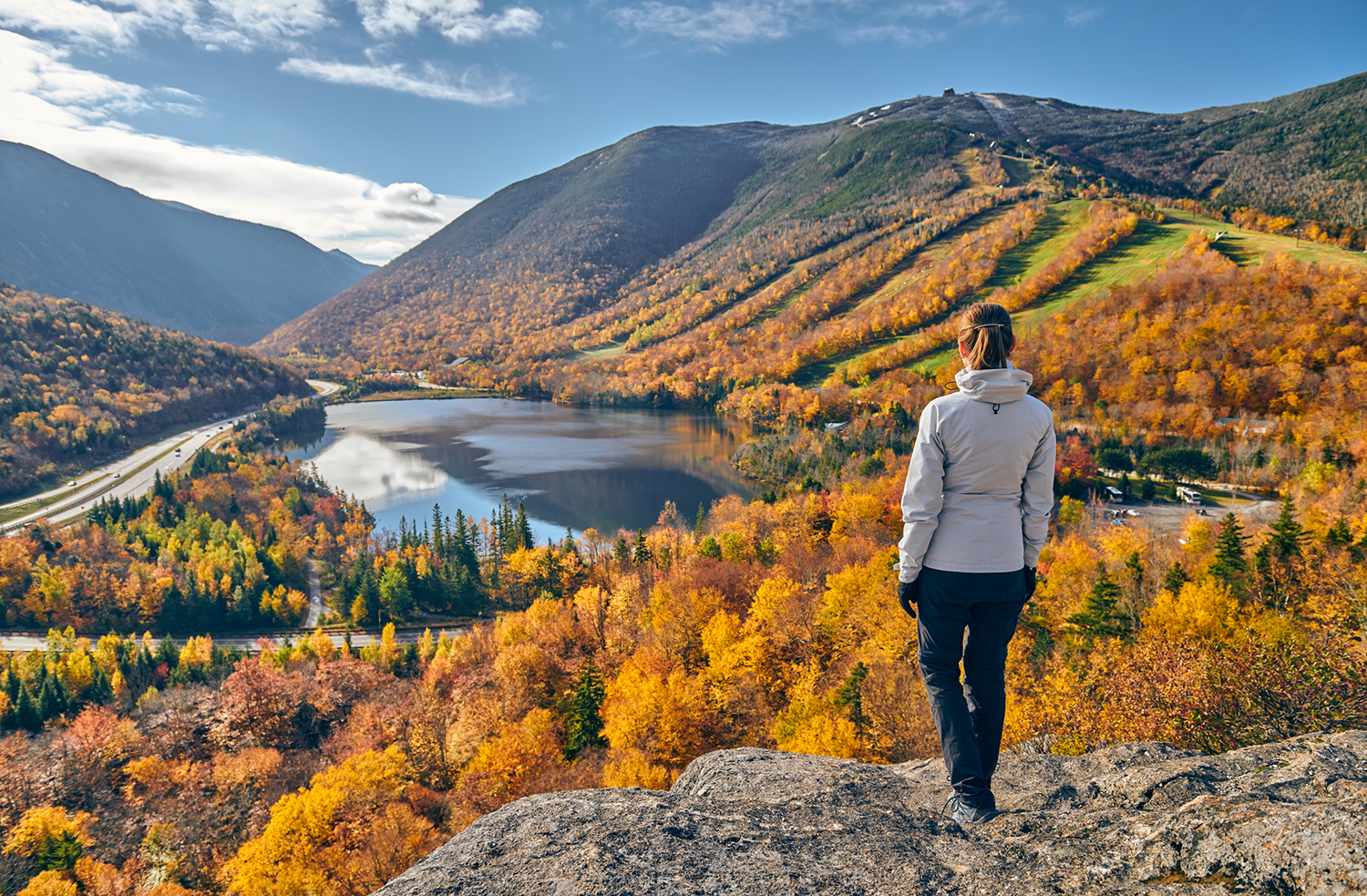 Woman hiking on rocky overlook with fall forests spread out below.