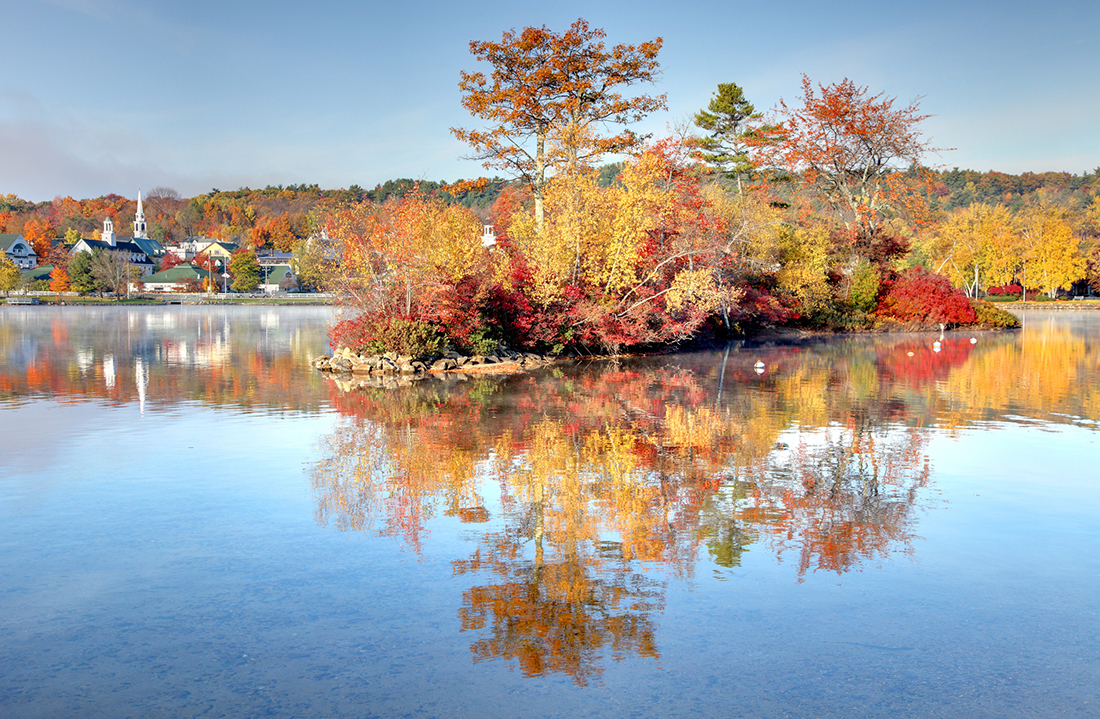 Autumn foliage on a lake with a white church and steeple on the opposite bank.