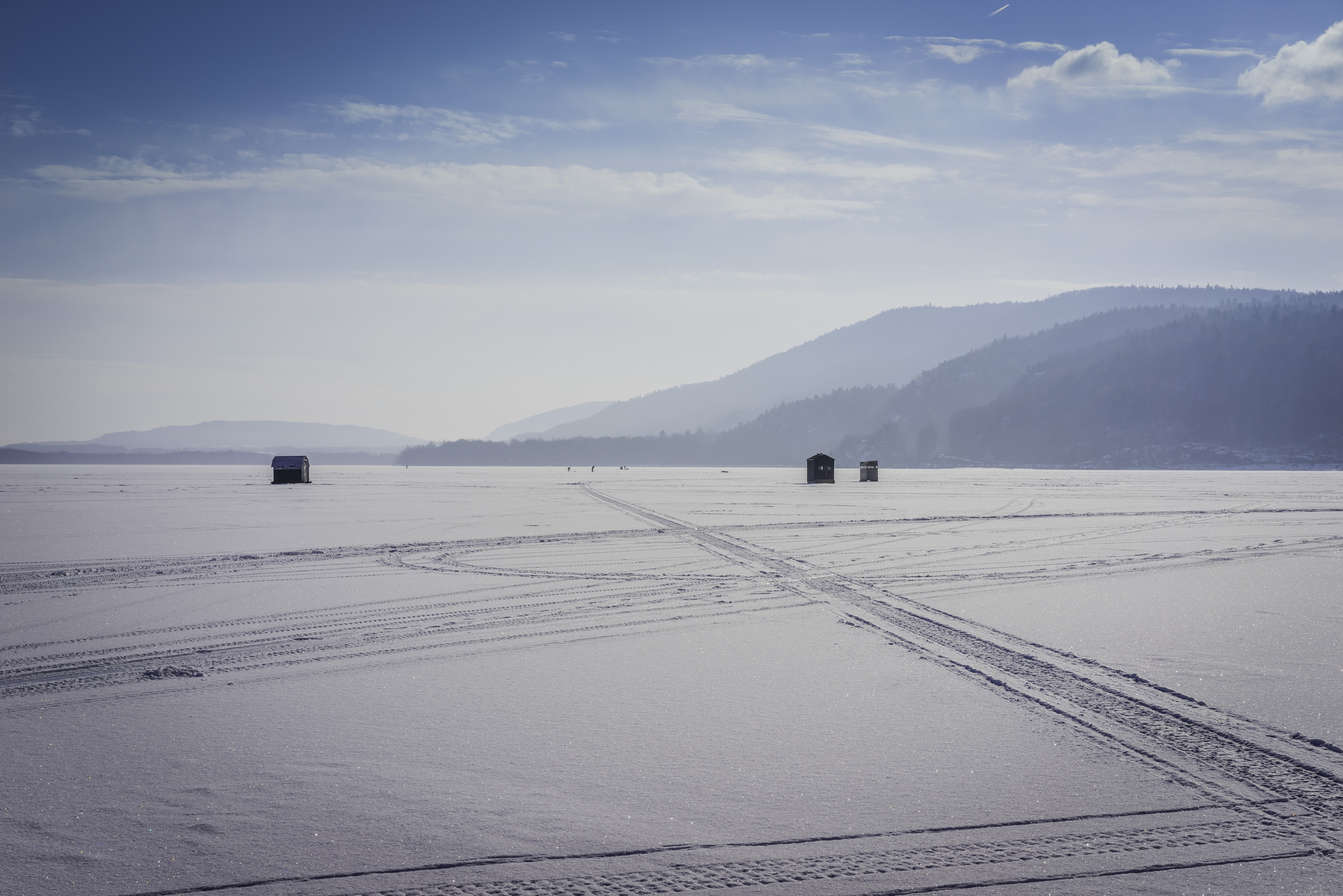 Ice fishing shanties sit in the distance on a frozen lake.
