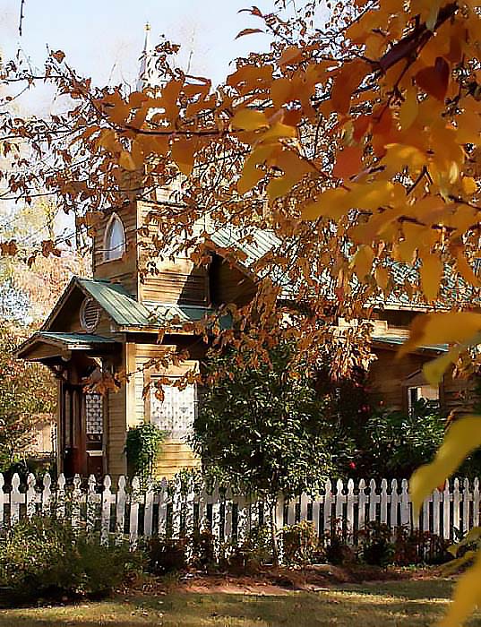 Wooden Christian chapel behind white picket fence.