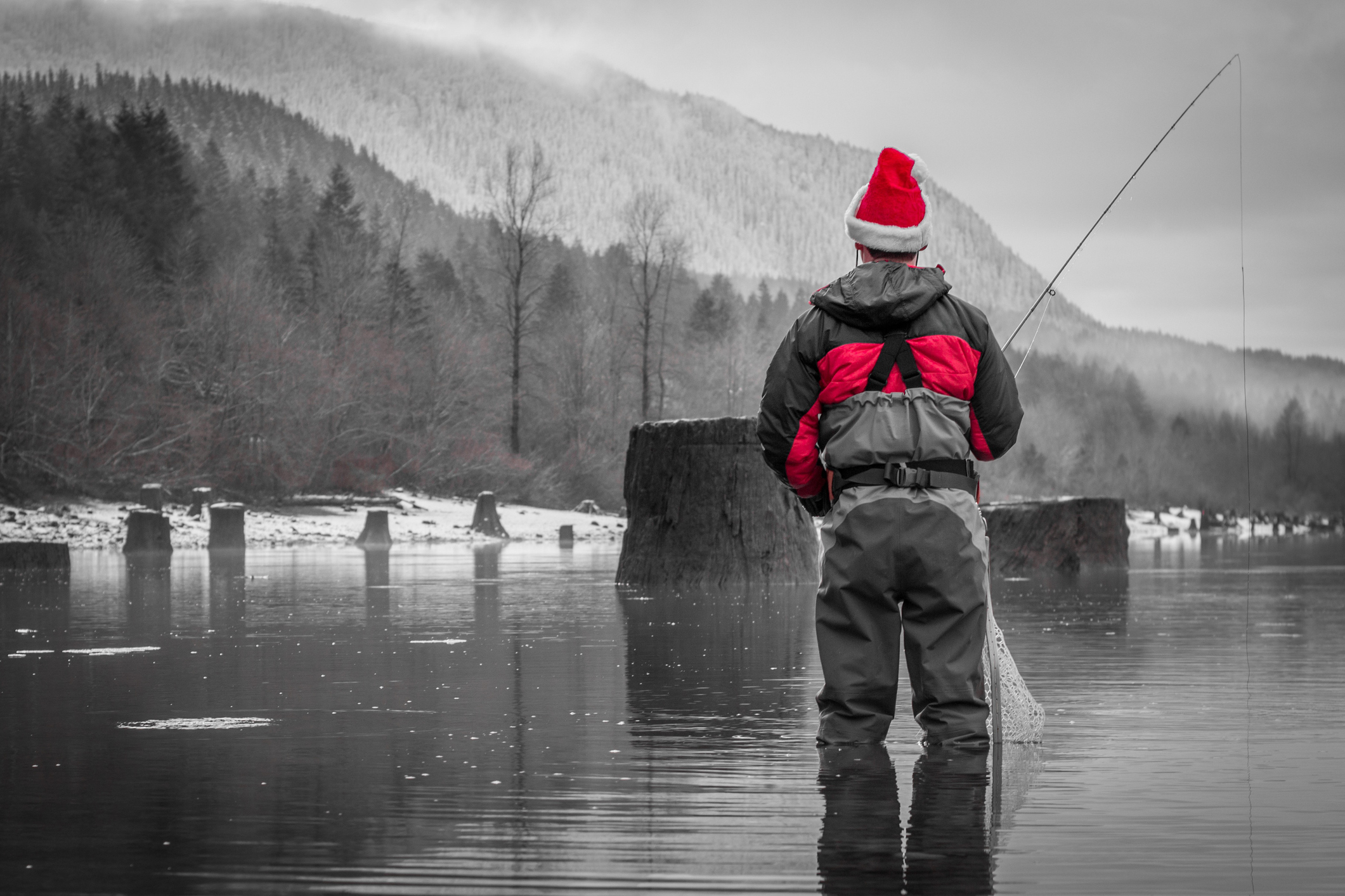 Man with santa hat and wader fishing against a snowy landscape.