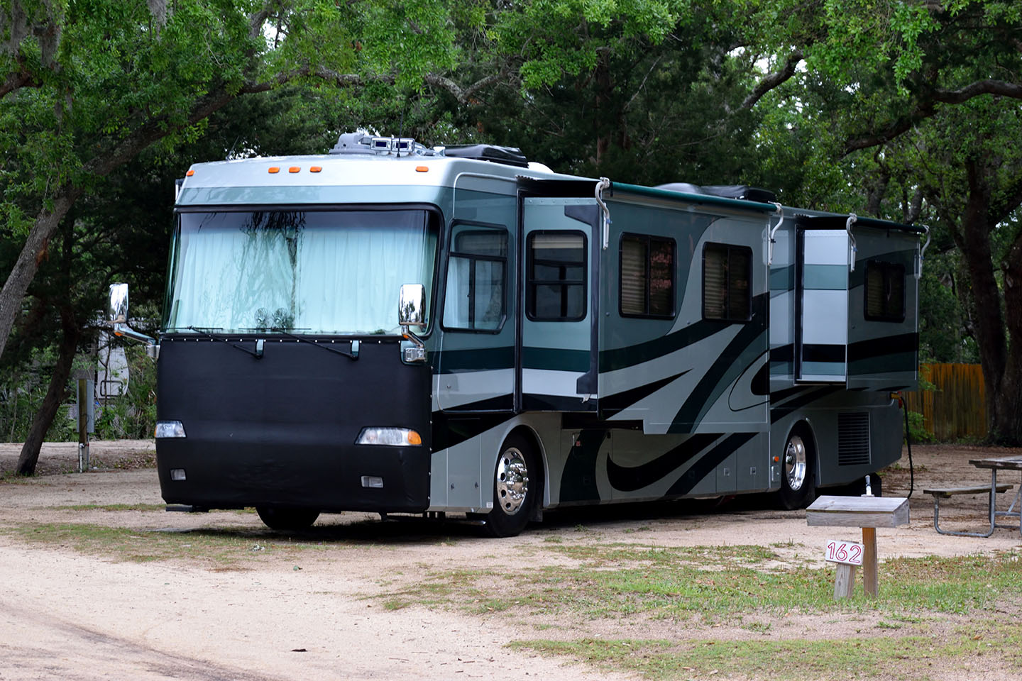 A motorhome with 2 slideouts deployed in a green campsite.
