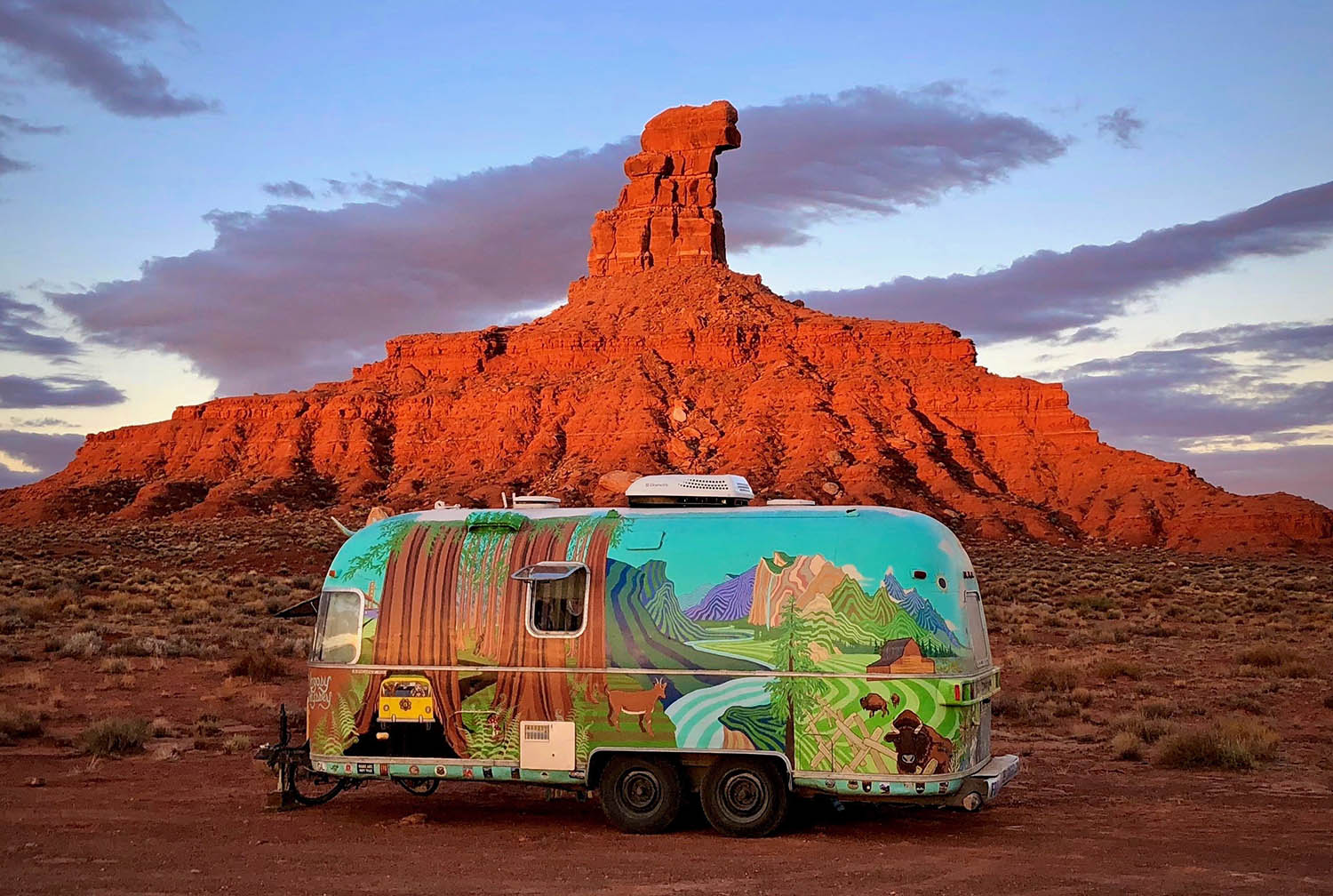 A rock spire thrusts toward the sky with a colorful trailer in foreground.