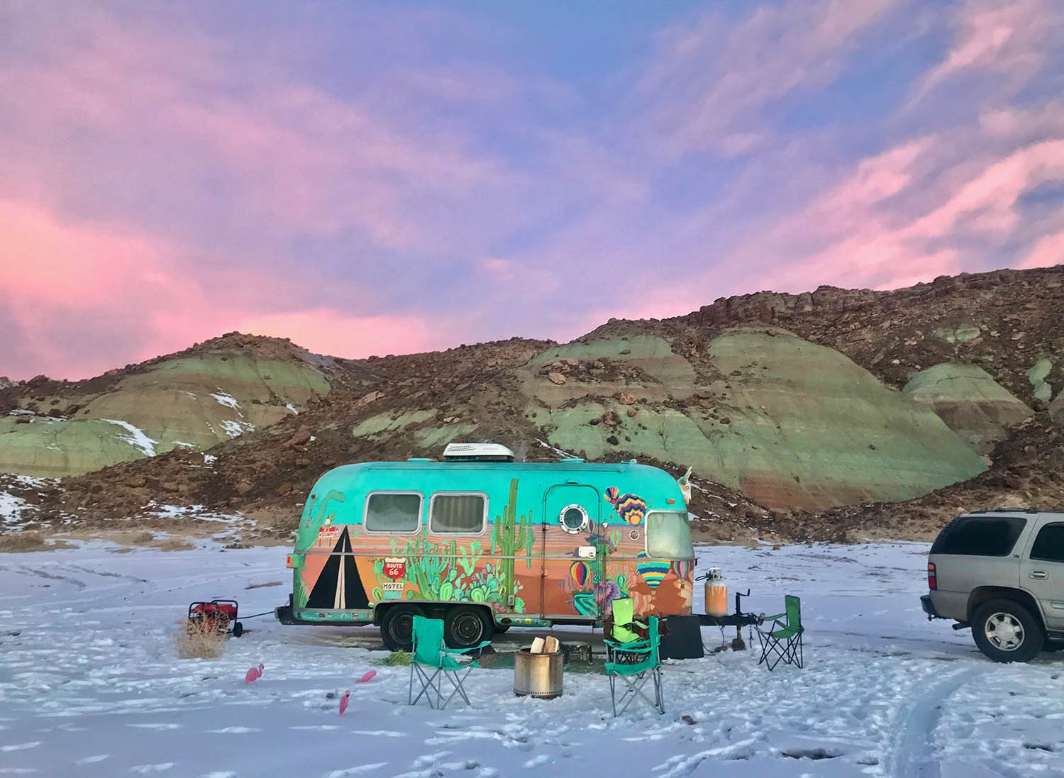A colorful Aistream RV parked on a snowy expanse with stone ridge in the background.