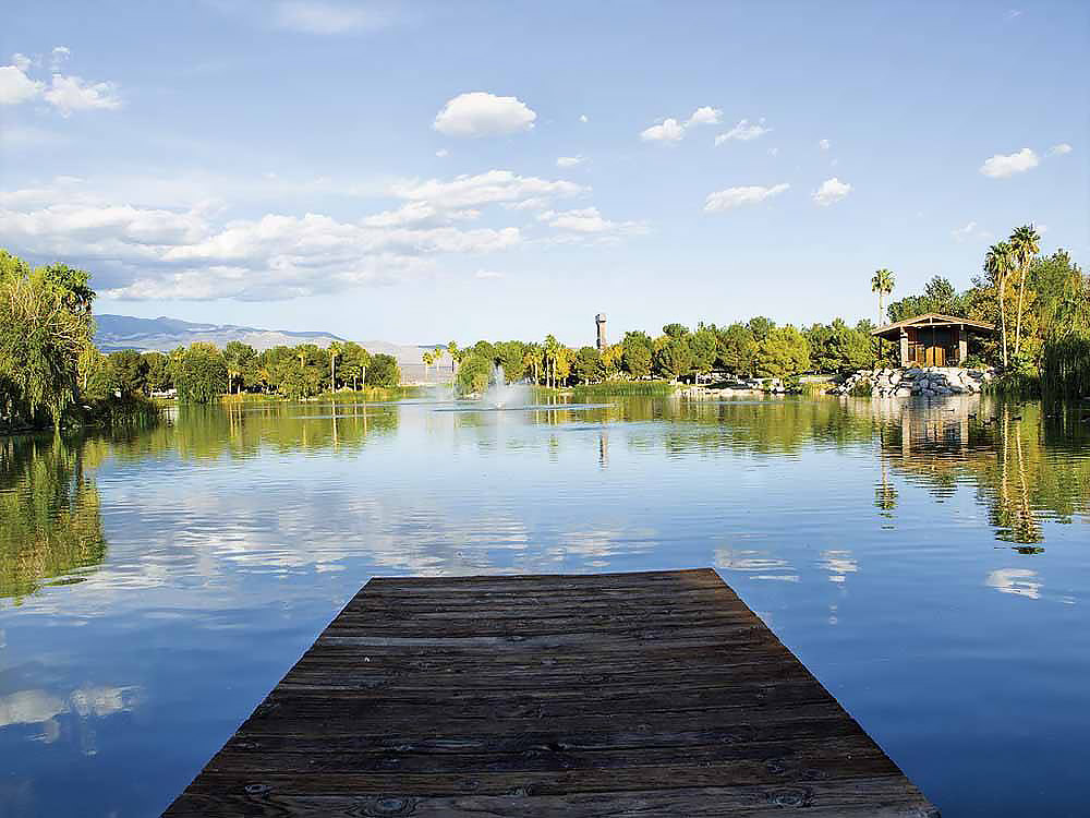 A dock overlooks a shimmering lake with a tower and house on the banks.
