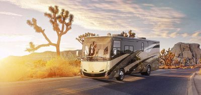 motorhome driving down a desert road with Joshua Trees in the background