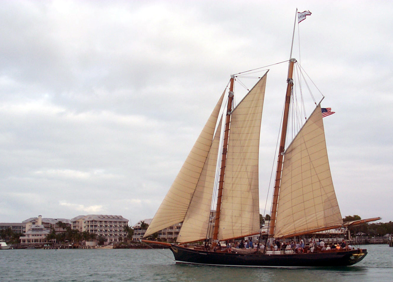 A two-masted boat sails off a coast.