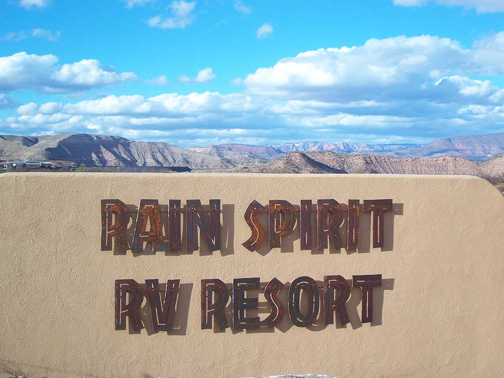 Sign declaring, "Rain Spirit RV Resort" with mountains in background.