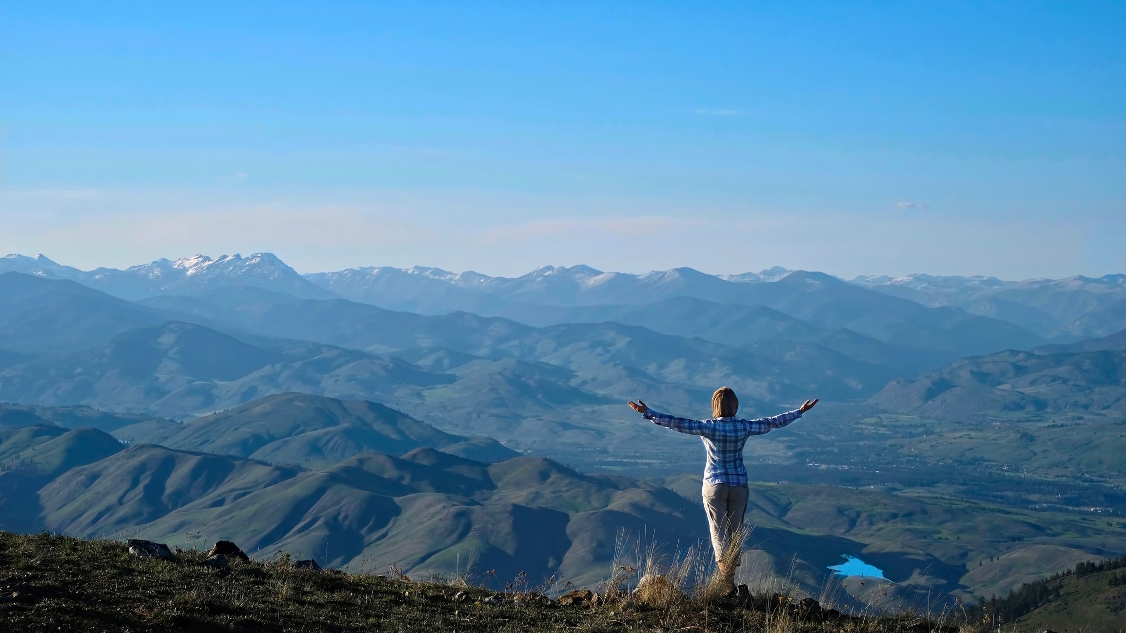 A woman spreads her arms as she gazes out over a vast mountain view.