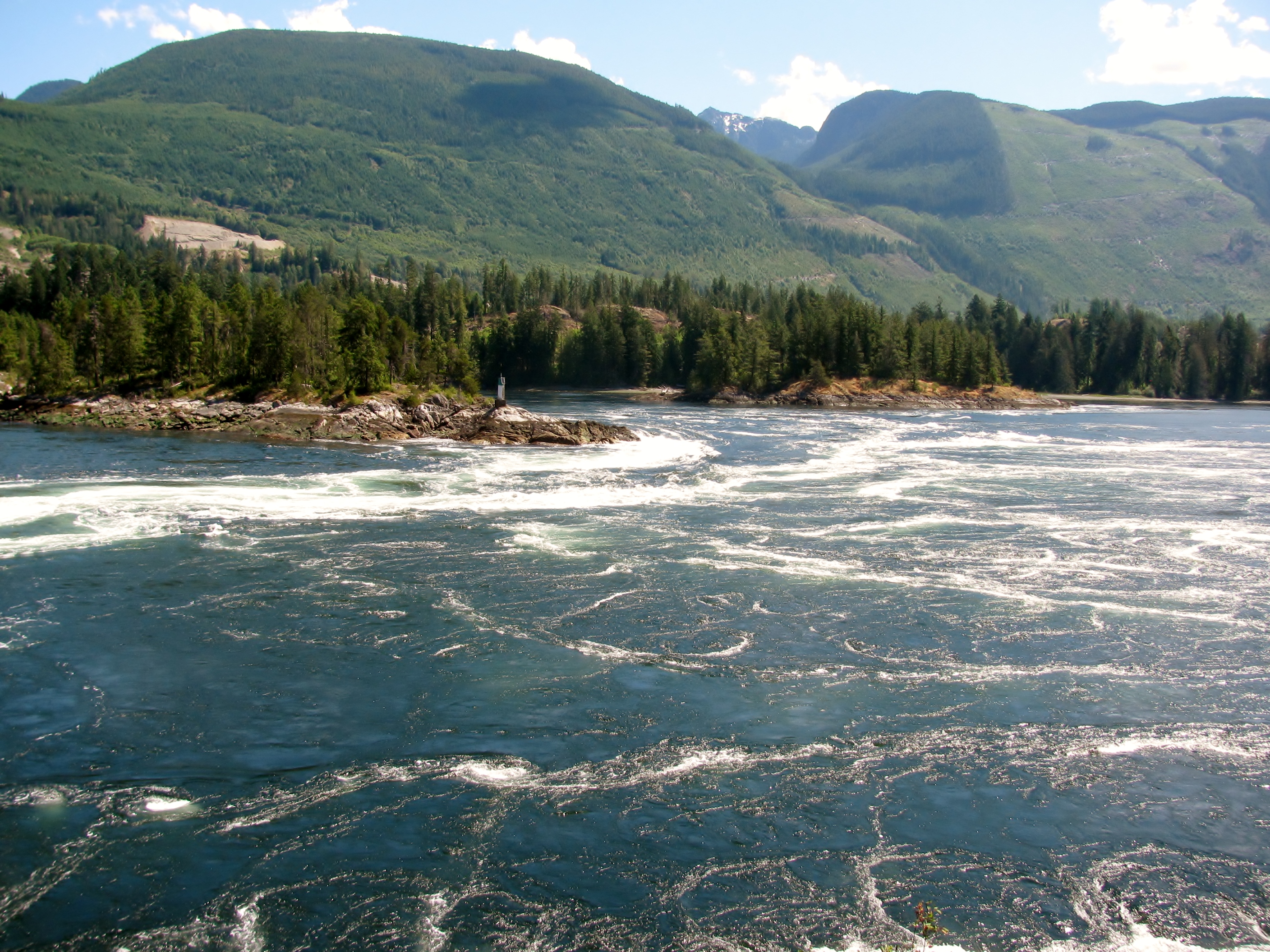 Rapids churn in a wide channel with green hills in the background.