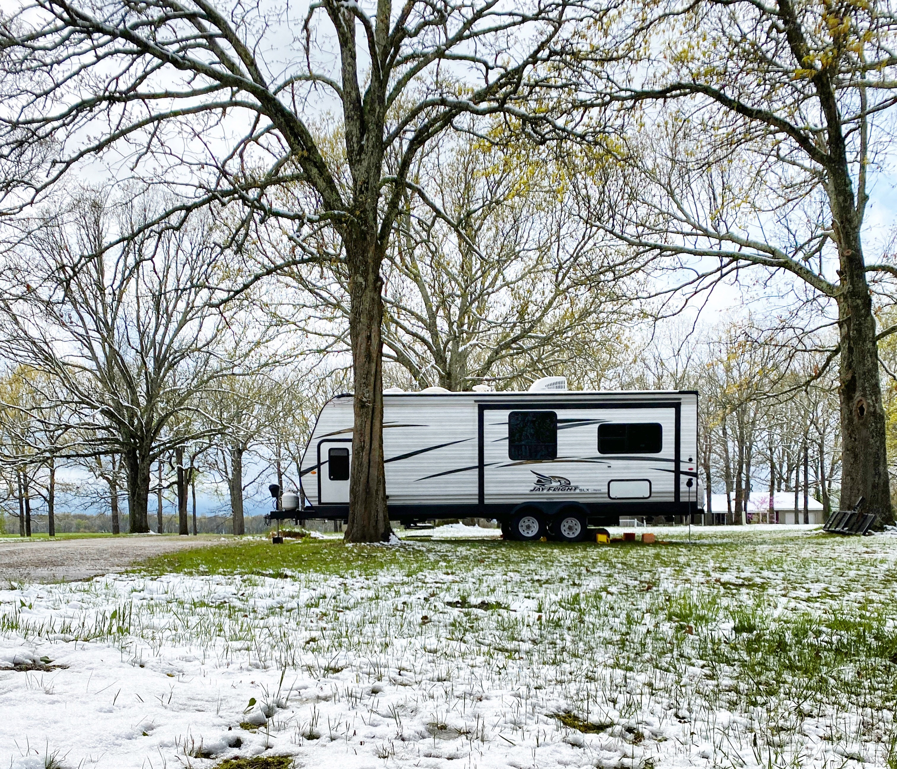 Travel trailer parked on a snowy meadow under spring trees.