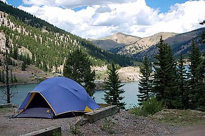 A blue dome tent on the banks of a lake.