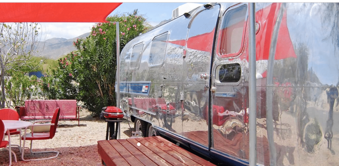 A vintage airstream parked in a site surrounded by vintage furniture.