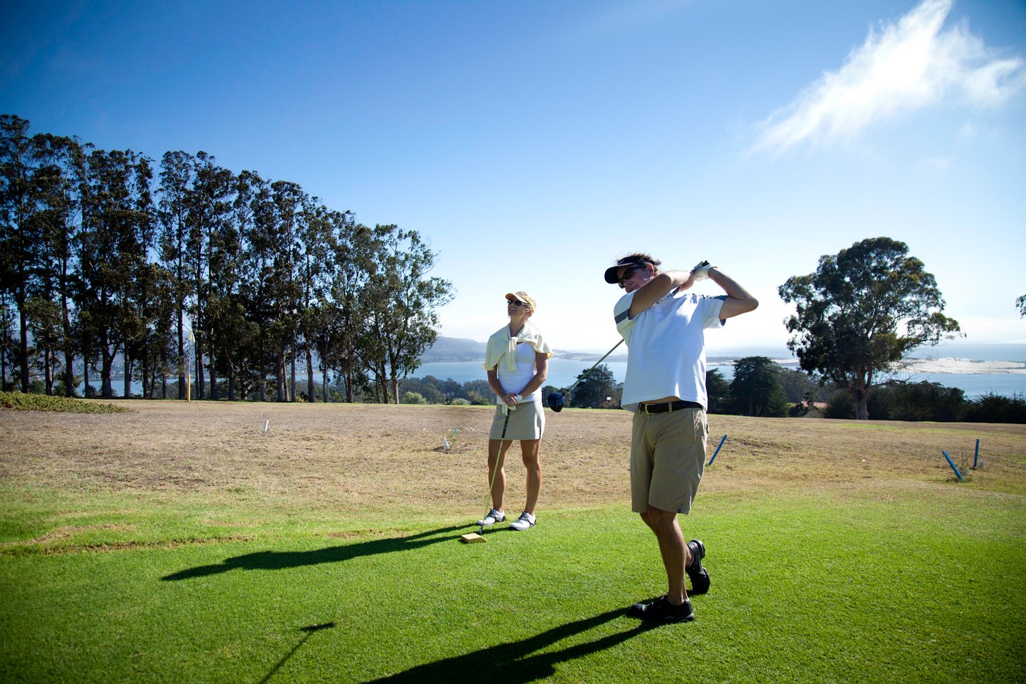 A golfer takes a swing on a course with a blue-sky background.