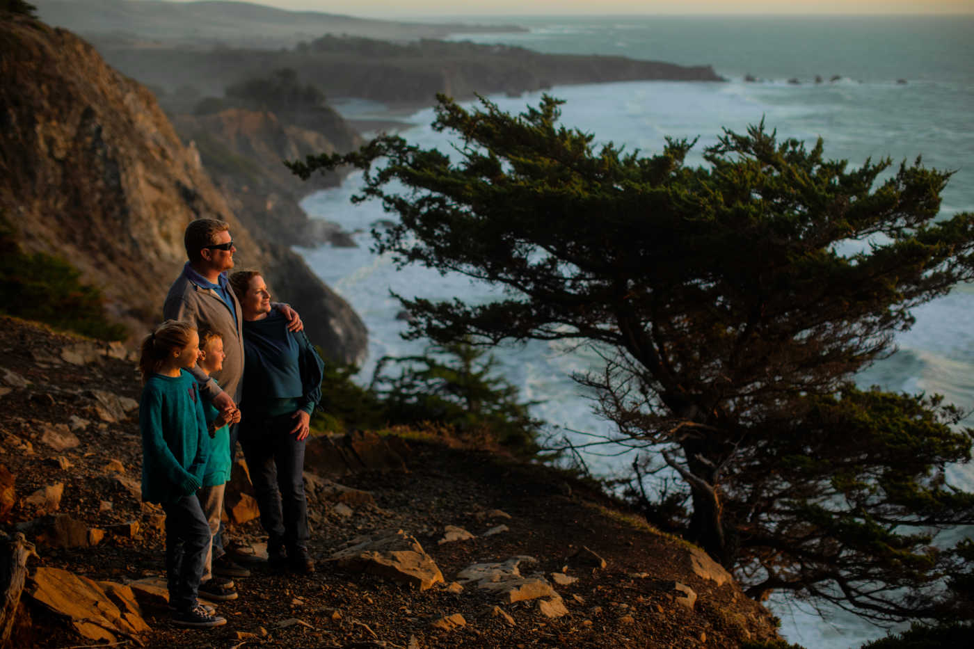 Four family members look out at the ocean from a clifftop perch.
