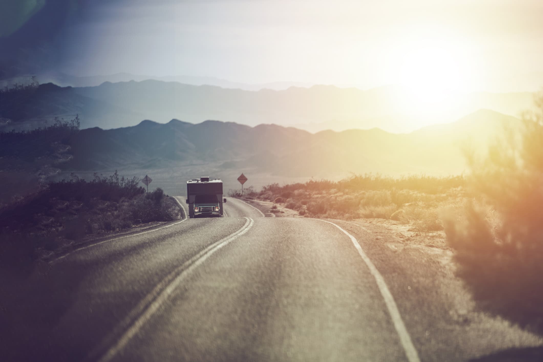 Motorhome driving on a sun-baked desert road.