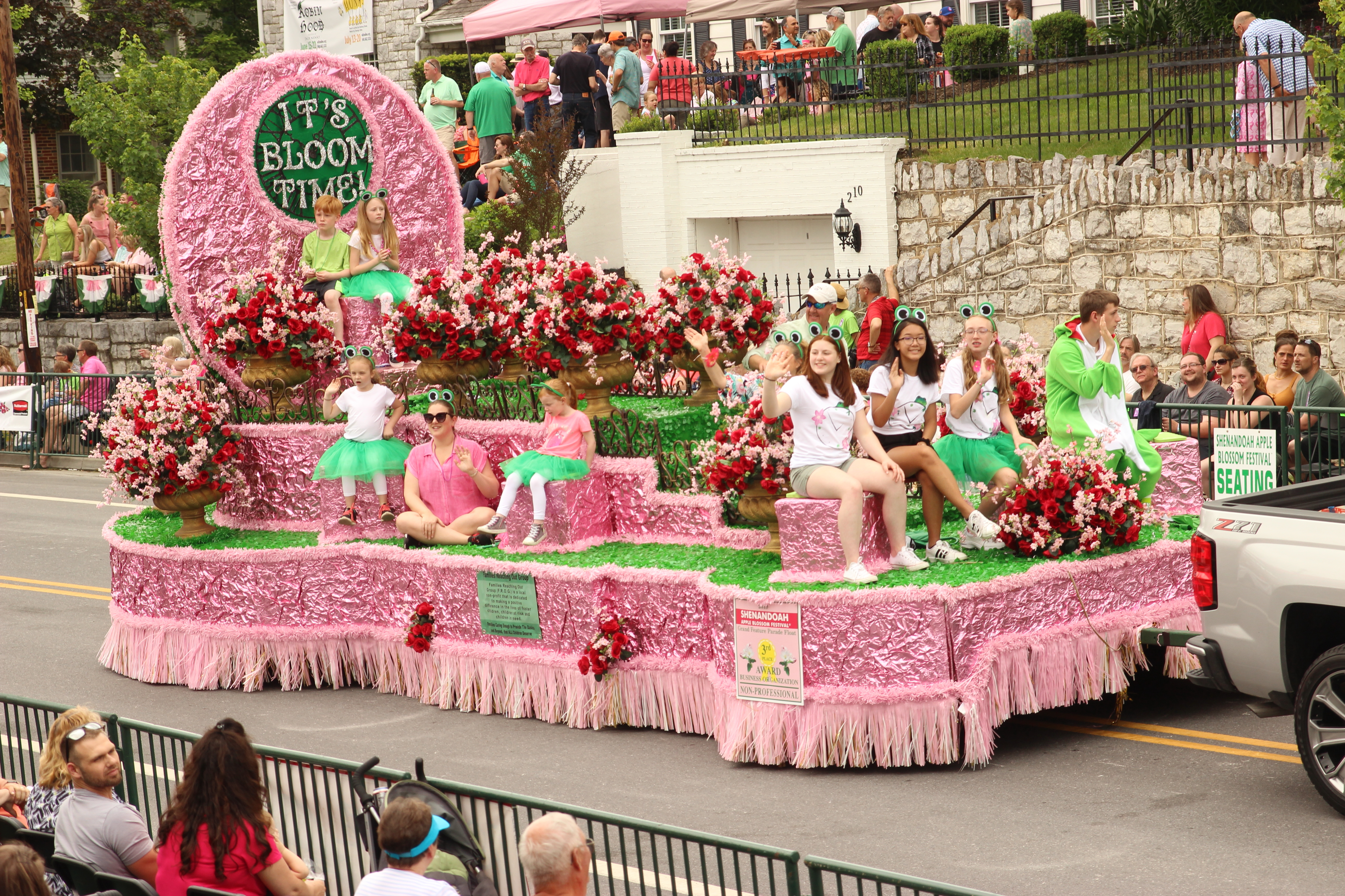 Kids ride on a pink float with sign announcing "it's bloom time!"