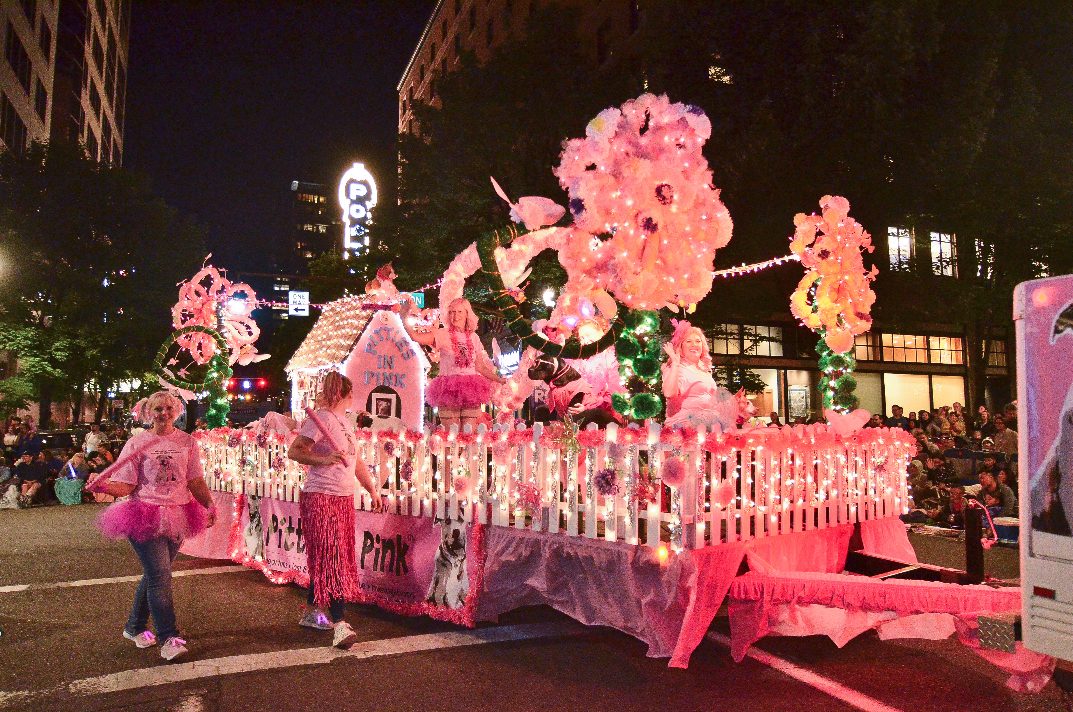 A pink float bedecked with roses rolls down the street accompanied by marchers.
