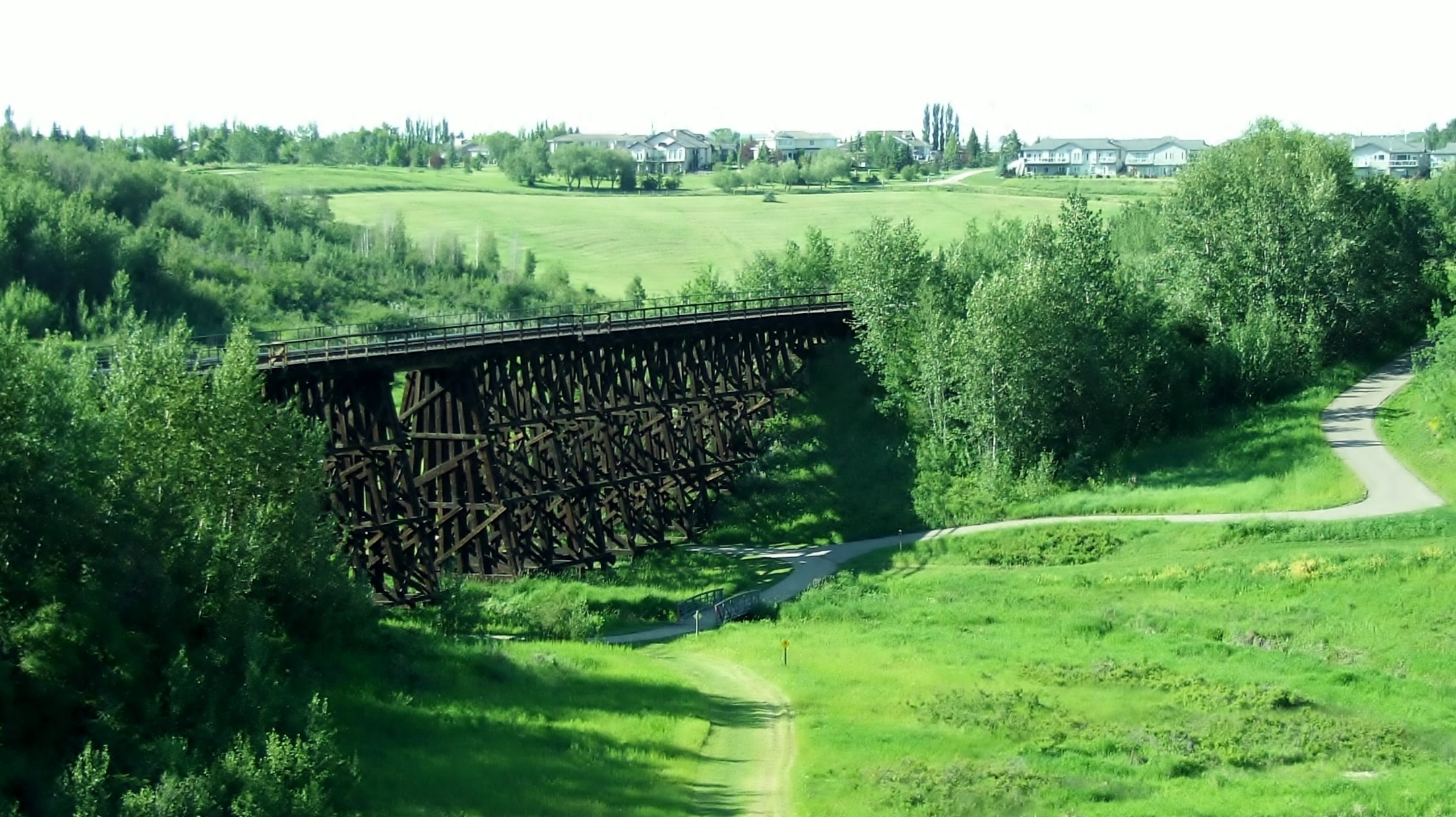 A wooden railroad trestle with a trail on the bround far below.