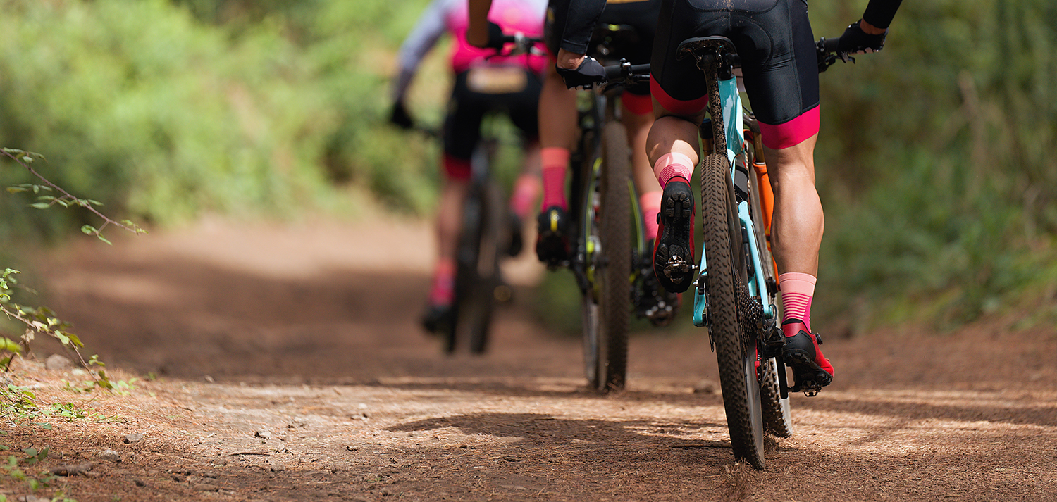 People biking down a dirt path flanked with greenery.