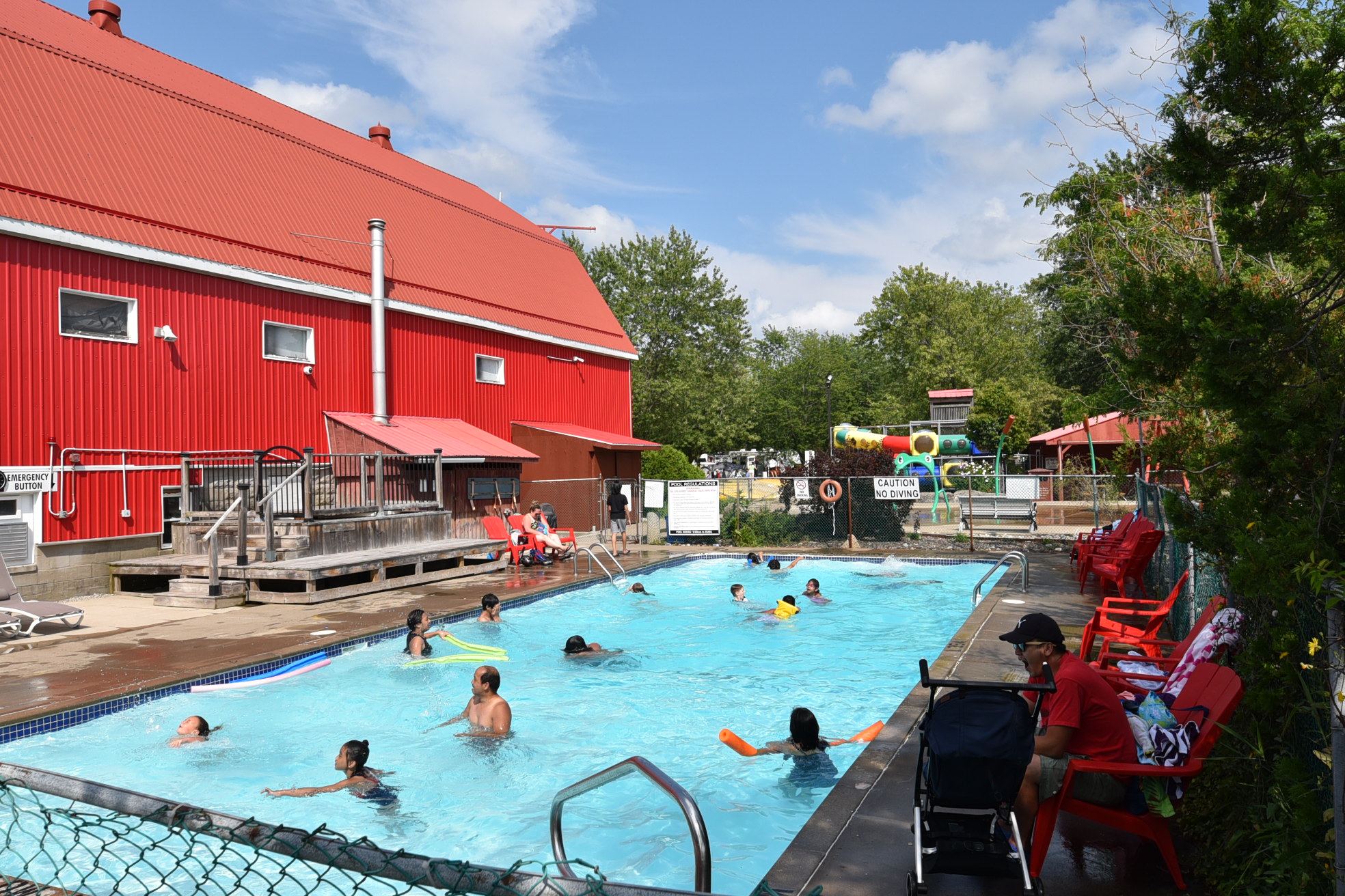 Families splash around in a rectangular swimming pool near a red barn-like structure.