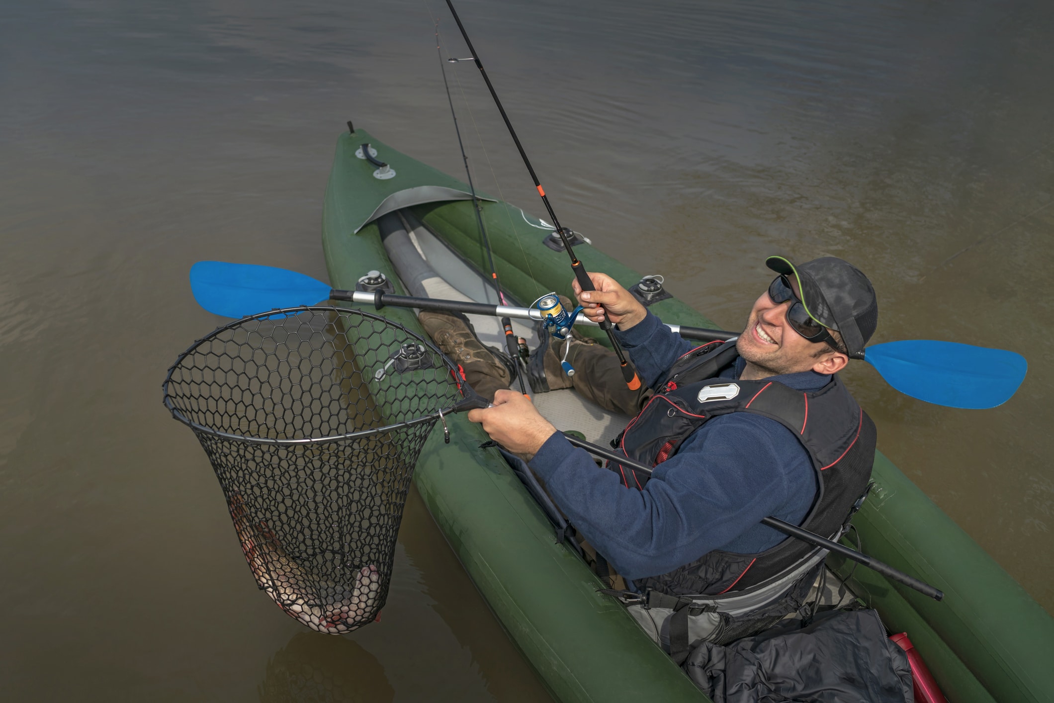 Kayak fishing at lake. Fisherman caught pike fish on inflatable boat with fishing tackle.