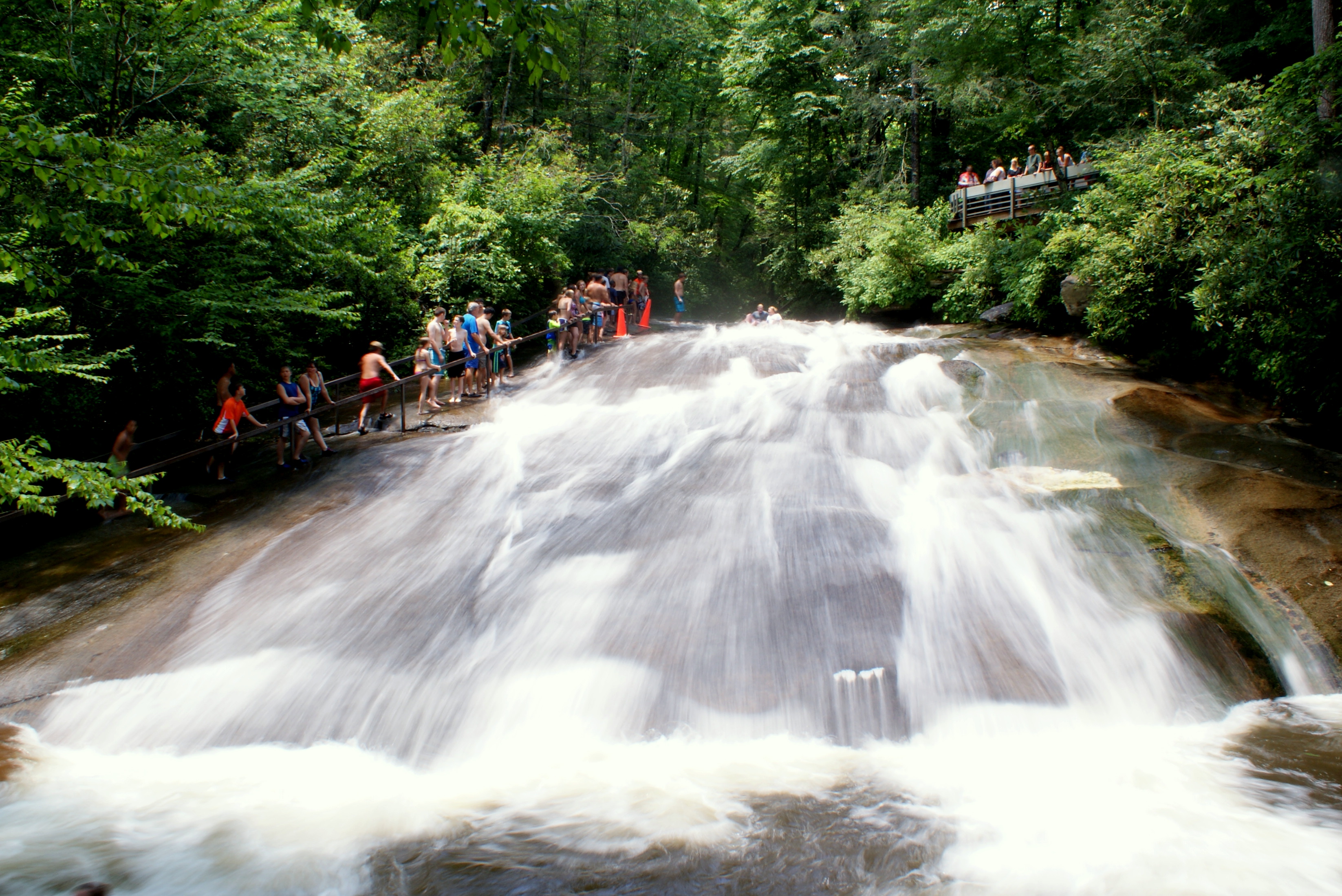 Water rushes down a smooth rock slope as bathers line up to ride it.