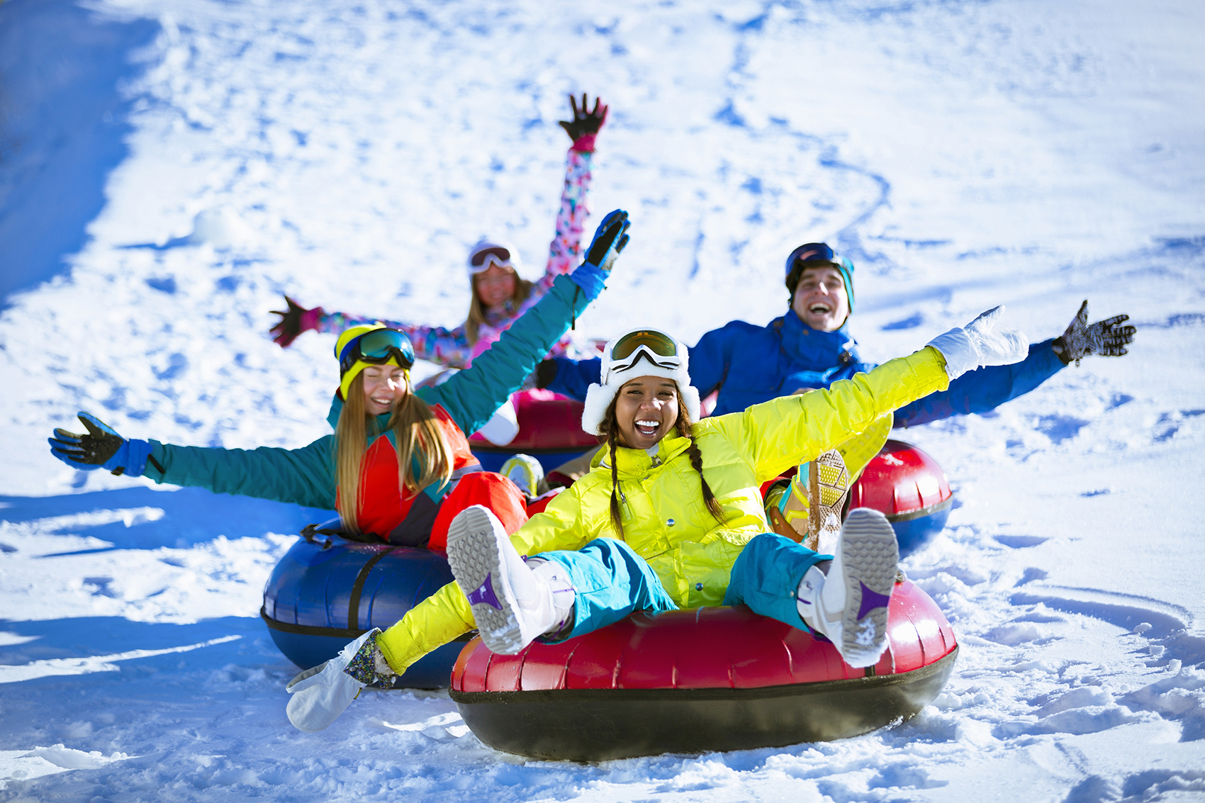 People in colorful jackets careening down a snowy slop on an inner tube.