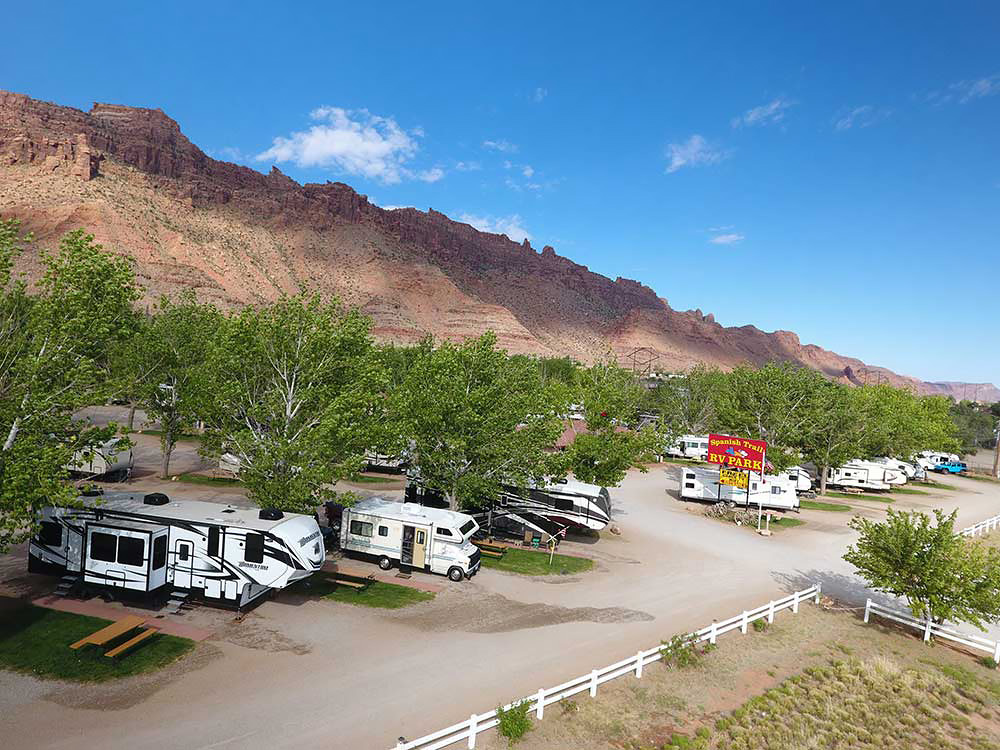 RVs parked on a row of spaces at the foot of a rugged desert slope.