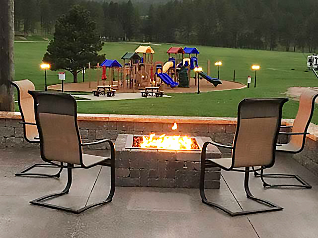 Chairs arrayed around a fire pit at dusk with play structures in the background.