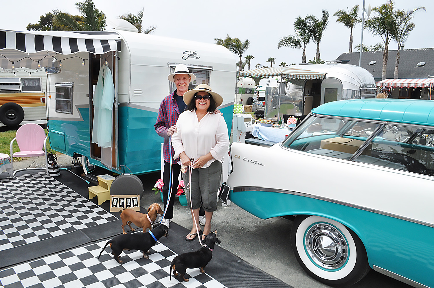 Couple pose in front of light blue sedan and trailer.