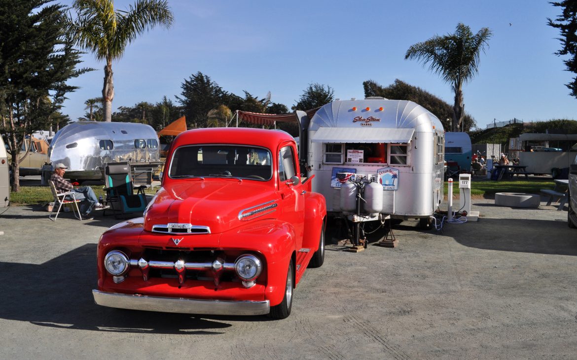 Red 50s pickup truck parked near a silver bullet trailer.