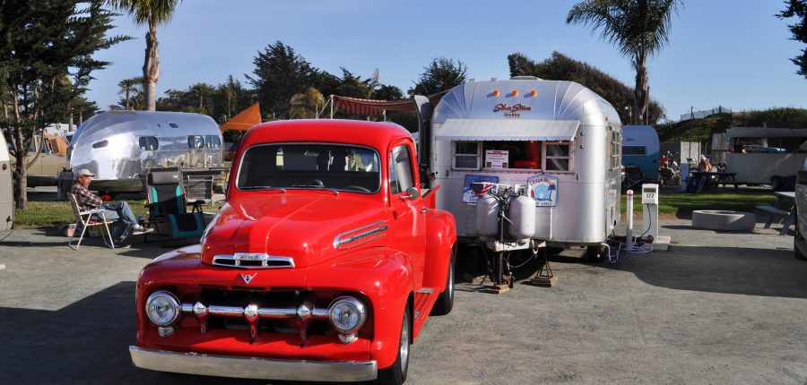 Red 50s pickup truck parked near a silver bullet trailer.