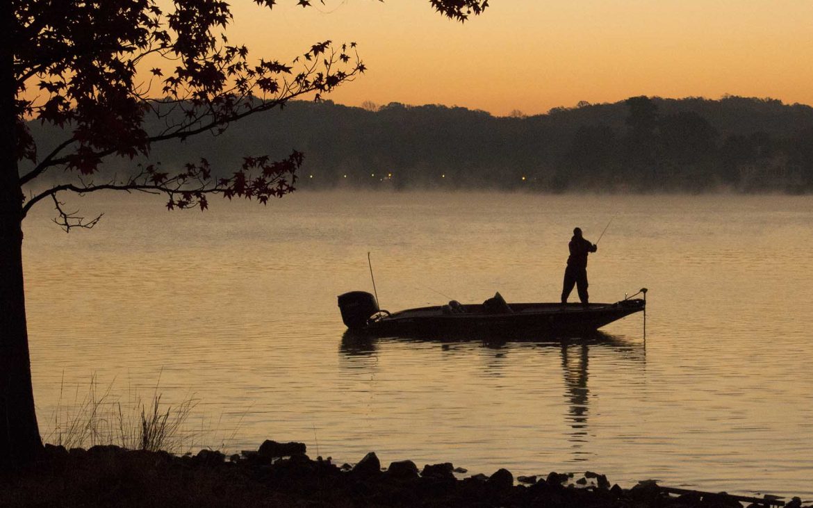 Silhouette of man fishing on a mist-covered lake.